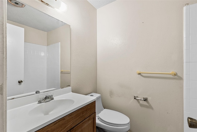 bathroom with a textured wall, vanity, toilet, and a textured ceiling