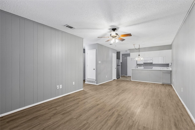 unfurnished living room with baseboards, visible vents, wood finished floors, and ceiling fan with notable chandelier