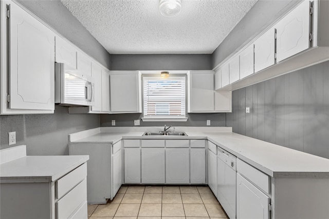 kitchen with white appliances, light tile patterned floors, a peninsula, white cabinetry, and a sink