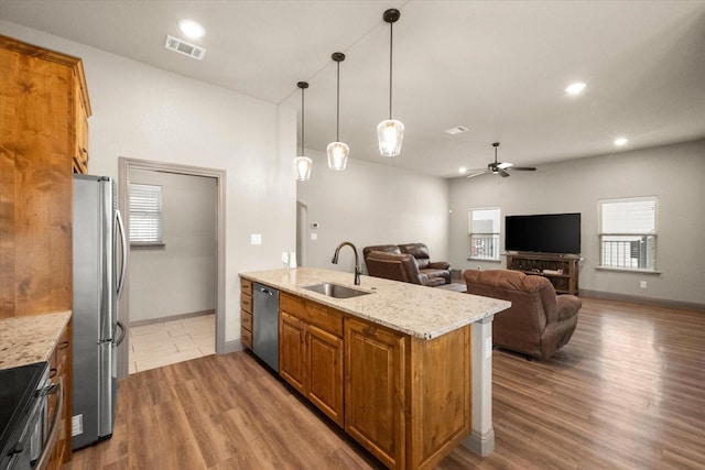 kitchen with light stone counters, brown cabinets, stainless steel appliances, hanging light fixtures, and a sink