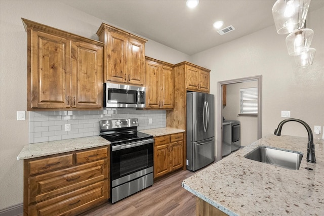 kitchen with visible vents, washer and clothes dryer, appliances with stainless steel finishes, a sink, and backsplash