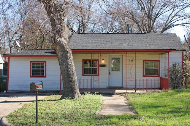 view of front facade with a front yard, a porch, and roof with shingles