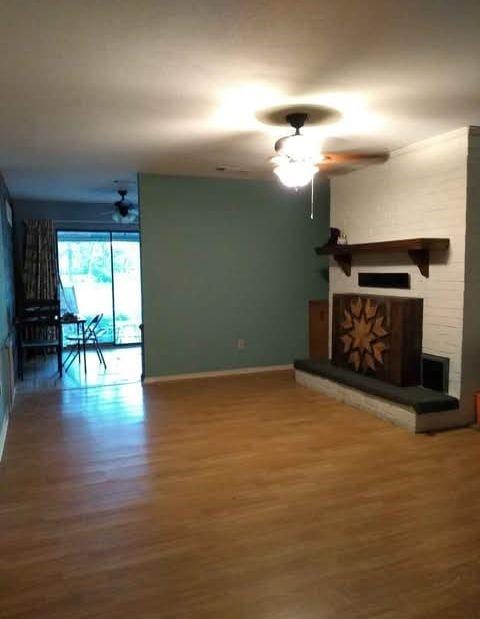 unfurnished living room with baseboards, wood finished floors, a ceiling fan, and a stone fireplace