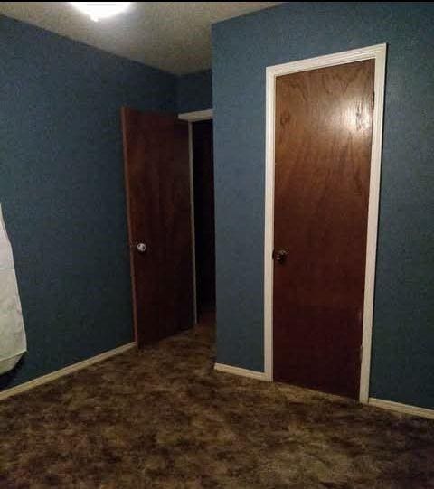 unfurnished bedroom with dark carpet and baseboards