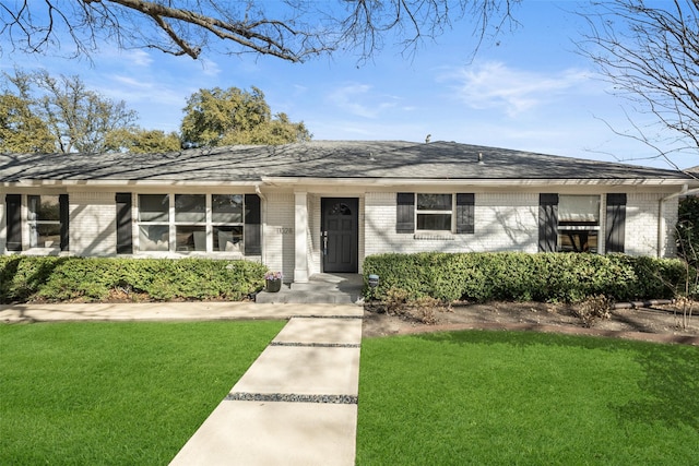 view of front facade featuring a shingled roof, a front yard, and brick siding