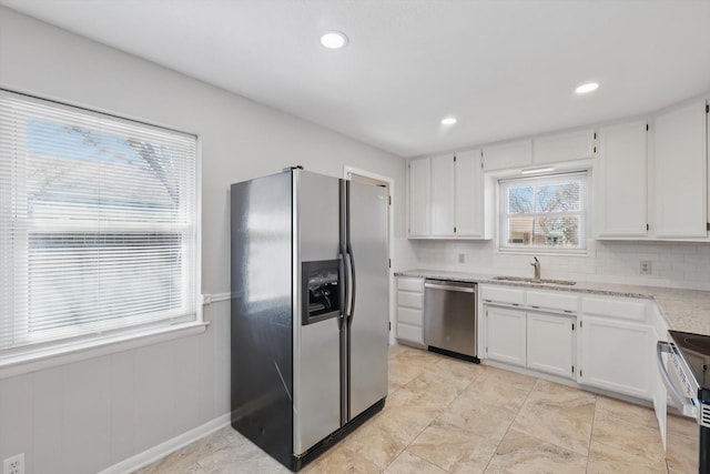 kitchen with appliances with stainless steel finishes, white cabinets, a sink, and tasteful backsplash