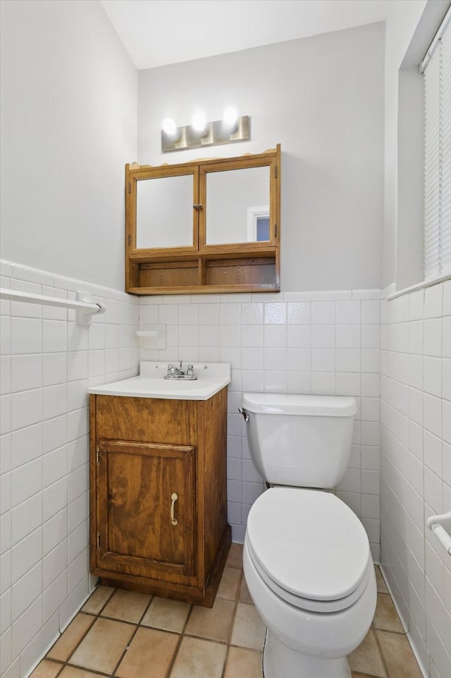 half bathroom featuring tile walls, toilet, wainscoting, vanity, and tile patterned flooring