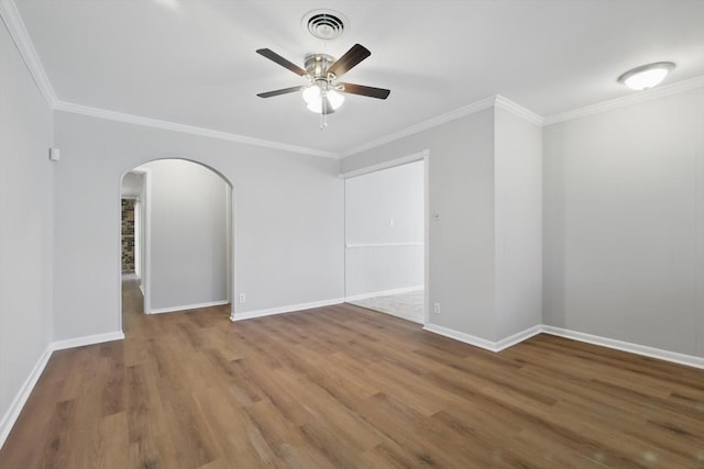 spare room featuring arched walkways, wood finished floors, visible vents, baseboards, and ornamental molding