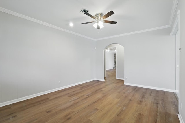 empty room with baseboards, arched walkways, ceiling fan, wood finished floors, and crown molding