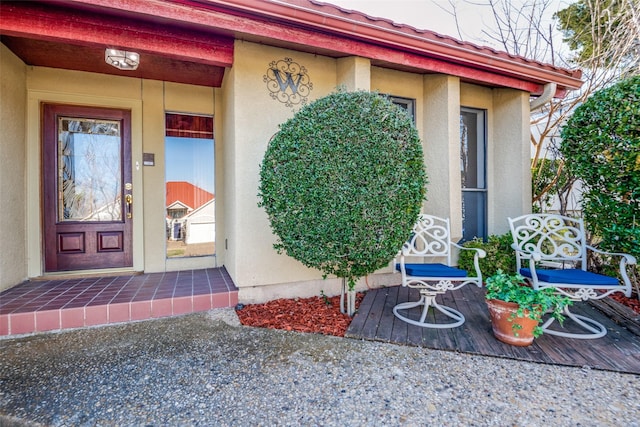 doorway to property featuring a porch, a tile roof, and stucco siding