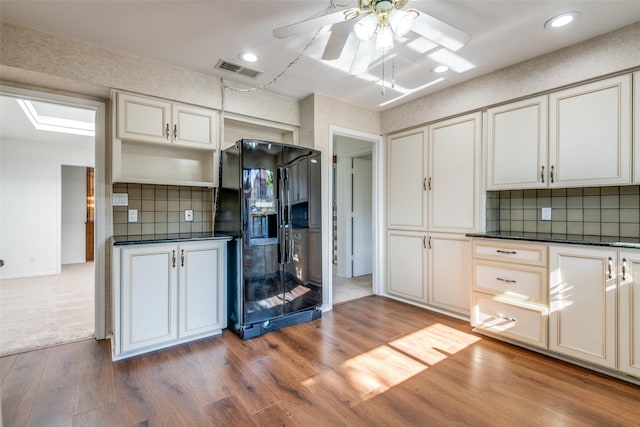 kitchen with dark countertops, visible vents, black refrigerator with ice dispenser, and wood finished floors