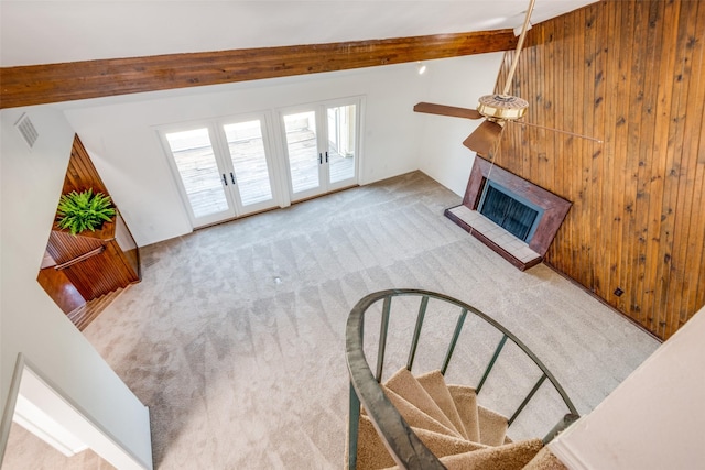 living room with lofted ceiling with beams, a fireplace with raised hearth, visible vents, french doors, and carpet