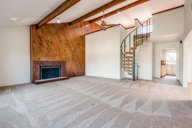 unfurnished living room featuring a large fireplace, beam ceiling, carpet flooring, and wood walls