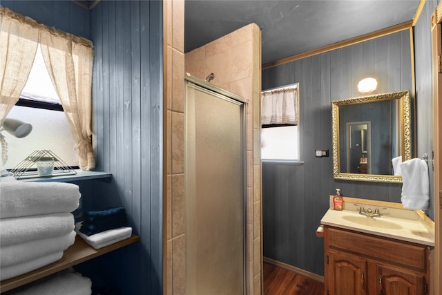 bathroom with wooden walls, wood finished floors, vanity, a shower stall, and crown molding