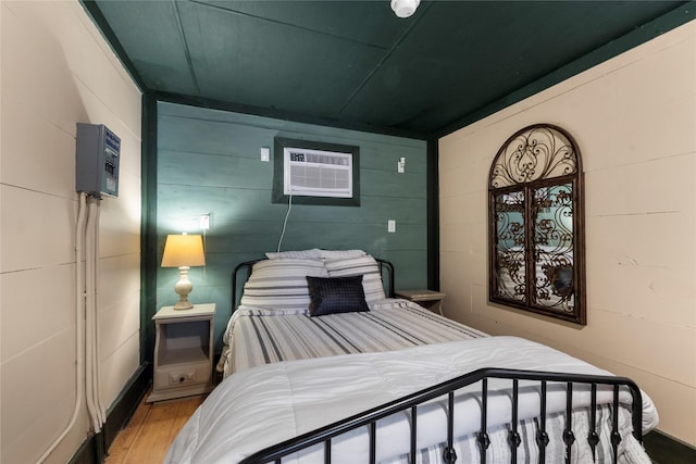 bedroom featuring light wood-type flooring, a wall unit AC, and concrete block wall