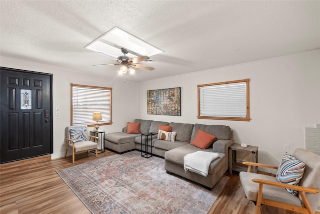 living area with a skylight, visible vents, a ceiling fan, a textured ceiling, and wood finished floors