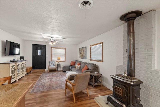 living area featuring visible vents, light wood-style floors, a wood stove, ceiling fan, and a textured ceiling