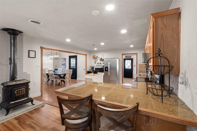 kitchen with visible vents, light wood-style flooring, a peninsula, a wood stove, and stainless steel refrigerator with ice dispenser