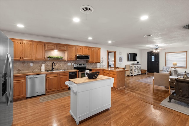 kitchen with stainless steel appliances, a peninsula, a sink, visible vents, and light wood finished floors