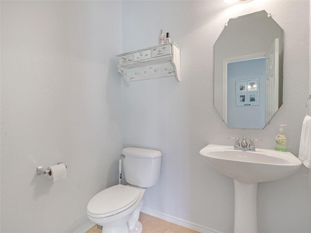 half bath with toilet, tile patterned flooring, baseboards, and a sink