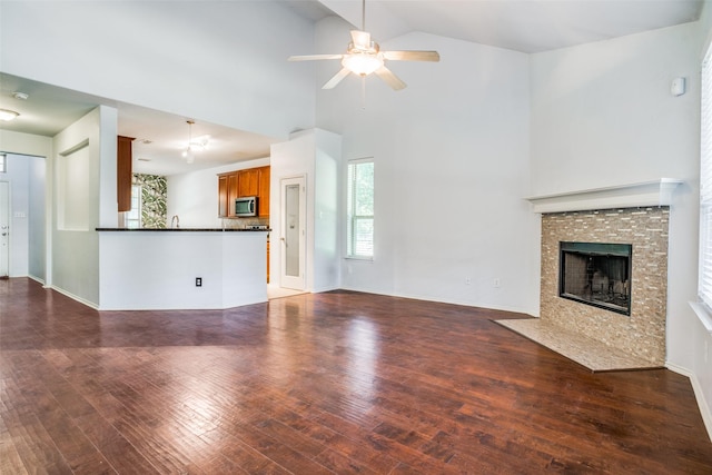 unfurnished living room featuring a tile fireplace, ceiling fan, wood finished floors, high vaulted ceiling, and a sink