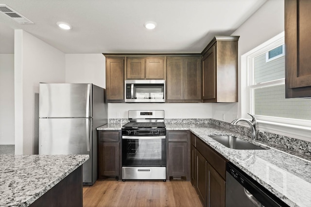 kitchen with light stone counters, light wood finished floors, visible vents, appliances with stainless steel finishes, and a sink