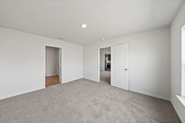 spare room with recessed lighting, carpet, visible vents, and baseboards