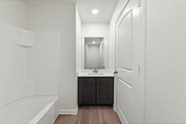 bathroom with baseboards, a textured wall, wood finished floors,  shower combination, and vanity