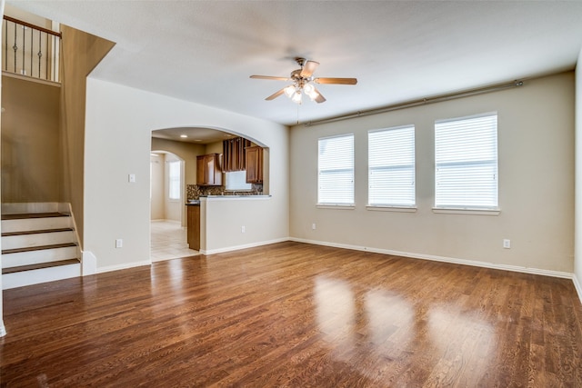 unfurnished living room with a ceiling fan, stairs, arched walkways, and wood finished floors