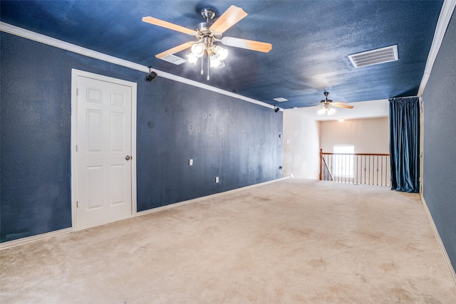 carpeted spare room featuring a textured ceiling, a ceiling fan, visible vents, and crown molding