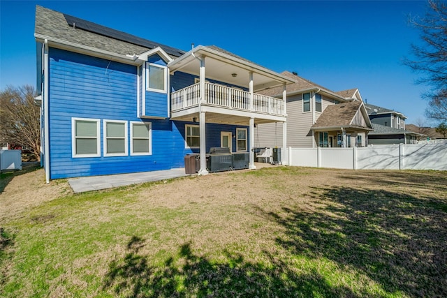 rear view of house with roof mounted solar panels, a lawn, a balcony, and fence