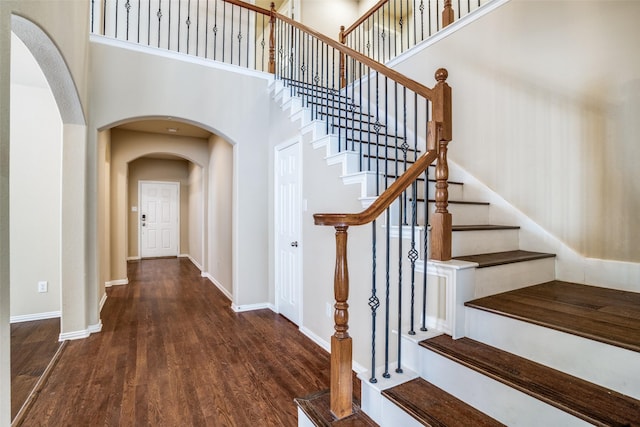 stairway with arched walkways, a towering ceiling, baseboards, and wood finished floors