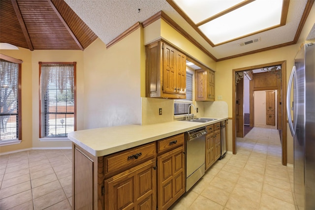 kitchen featuring brown cabinets, stainless steel appliances, crown molding, light countertops, and a sink