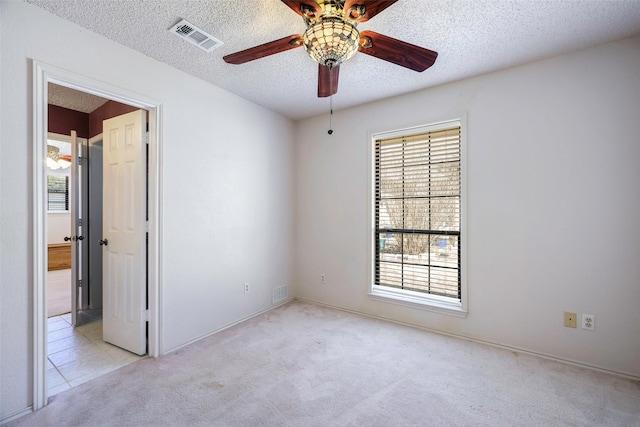 carpeted empty room with ceiling fan, visible vents, and a textured ceiling