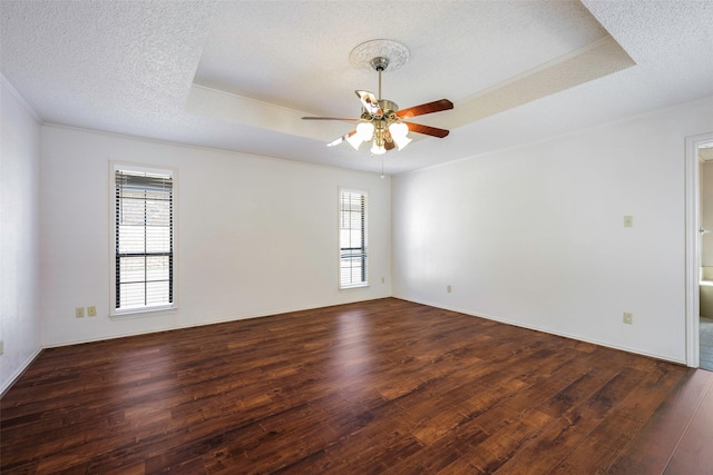 empty room with ceiling fan, a textured ceiling, a tray ceiling, and wood finished floors