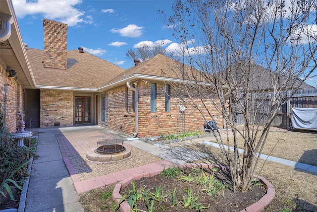 exterior space featuring brick siding, fence, french doors, roof with shingles, and a chimney