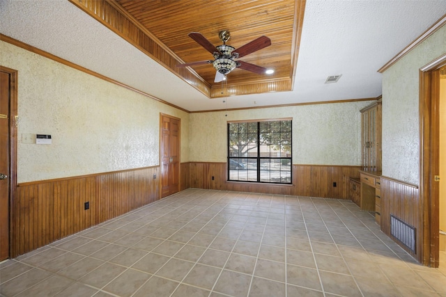 spare room with a raised ceiling, wainscoting, ceiling fan, and wood walls