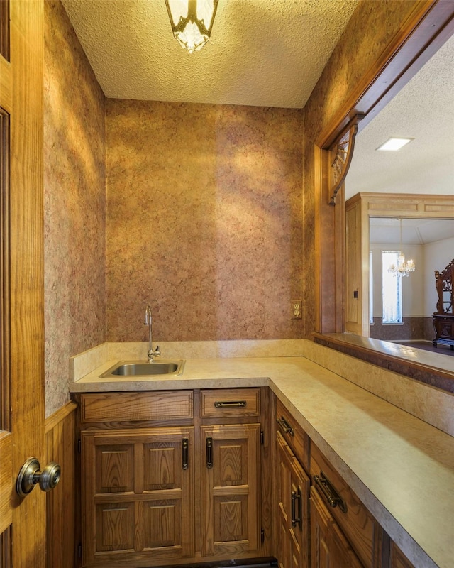 bathroom with a wainscoted wall, a sink, a textured ceiling, a chandelier, and wallpapered walls