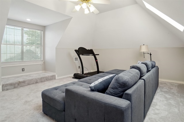 living room featuring vaulted ceiling with skylight, light colored carpet, ceiling fan, and baseboards