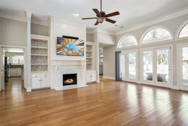 unfurnished living room featuring built in features, light wood-type flooring, a fireplace, and plenty of natural light