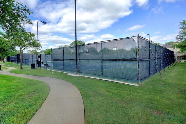 view of tennis court featuring fence and a lawn