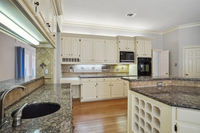 kitchen with light wood finished floors, visible vents, ornamental molding, black appliances, and a sink