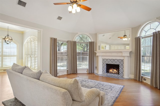 living area featuring a tile fireplace, visible vents, lofted ceiling, and wood finished floors