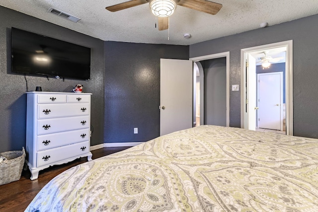 bedroom with visible vents, a textured wall, ceiling fan, dark wood-style flooring, and a textured ceiling