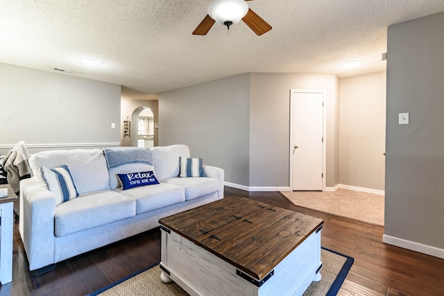 living room with a ceiling fan, arched walkways, dark wood finished floors, and a textured ceiling