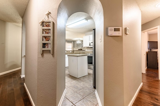 hall with a textured wall, a textured ceiling, and baseboards