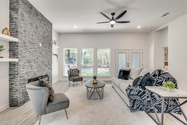 living area with french doors, visible vents, ceiling fan, a stone fireplace, and wood finished floors