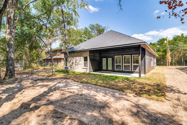 back of property with french doors, a shingled roof, and brick siding