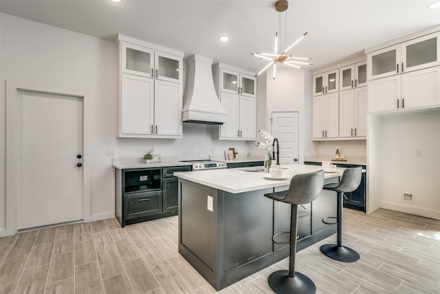 kitchen featuring white cabinets, light countertops, wood finish floors, premium range hood, and a sink