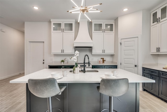 kitchen featuring an island with sink, a breakfast bar area, wood tiled floor, custom exhaust hood, and a sink